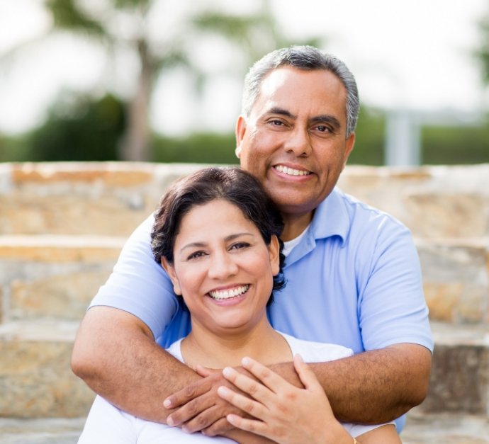 Smiling man hugging woman from behind with brick wall in background