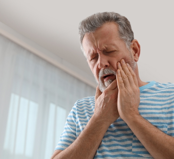 Older man wincing and holding his cheek in pain