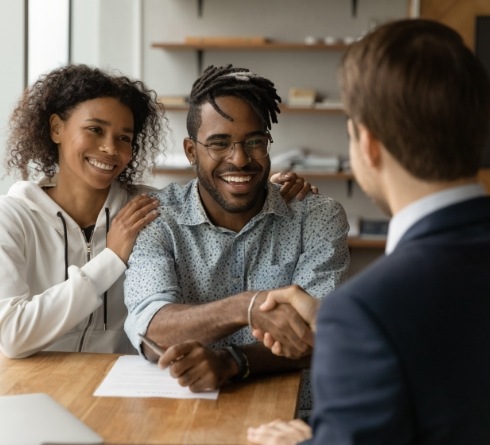 Smiling man shaking hands with person sitting across table