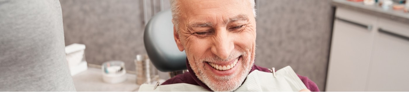 Senior man in dental chair smiling with implant dentures in Richardson