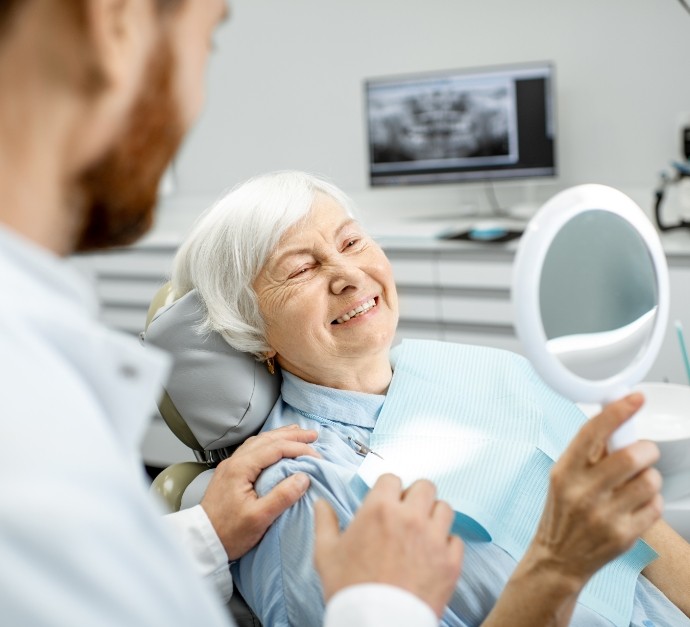 Senior dental patient admiring her smile in hand mirror