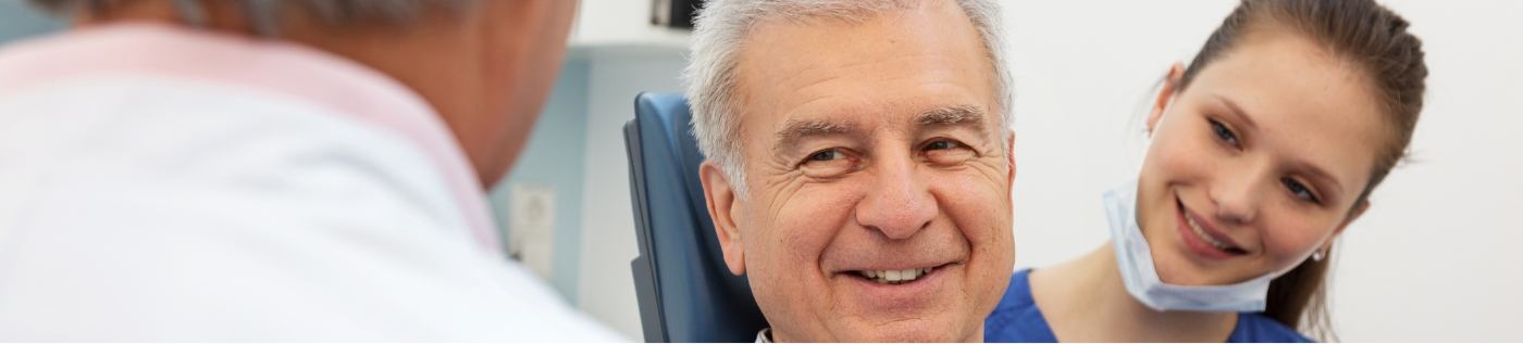 Senior man in treatment chair smiling at his oral surgery dentist in Richardson