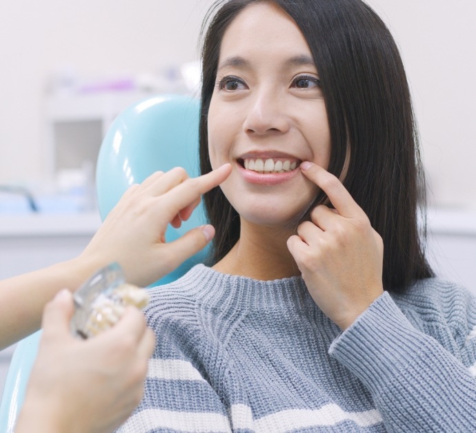 Woman in dental chair pointing to her smile