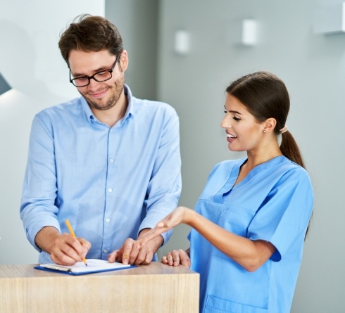 Dental team member showing a patient where to sign on a clipboard